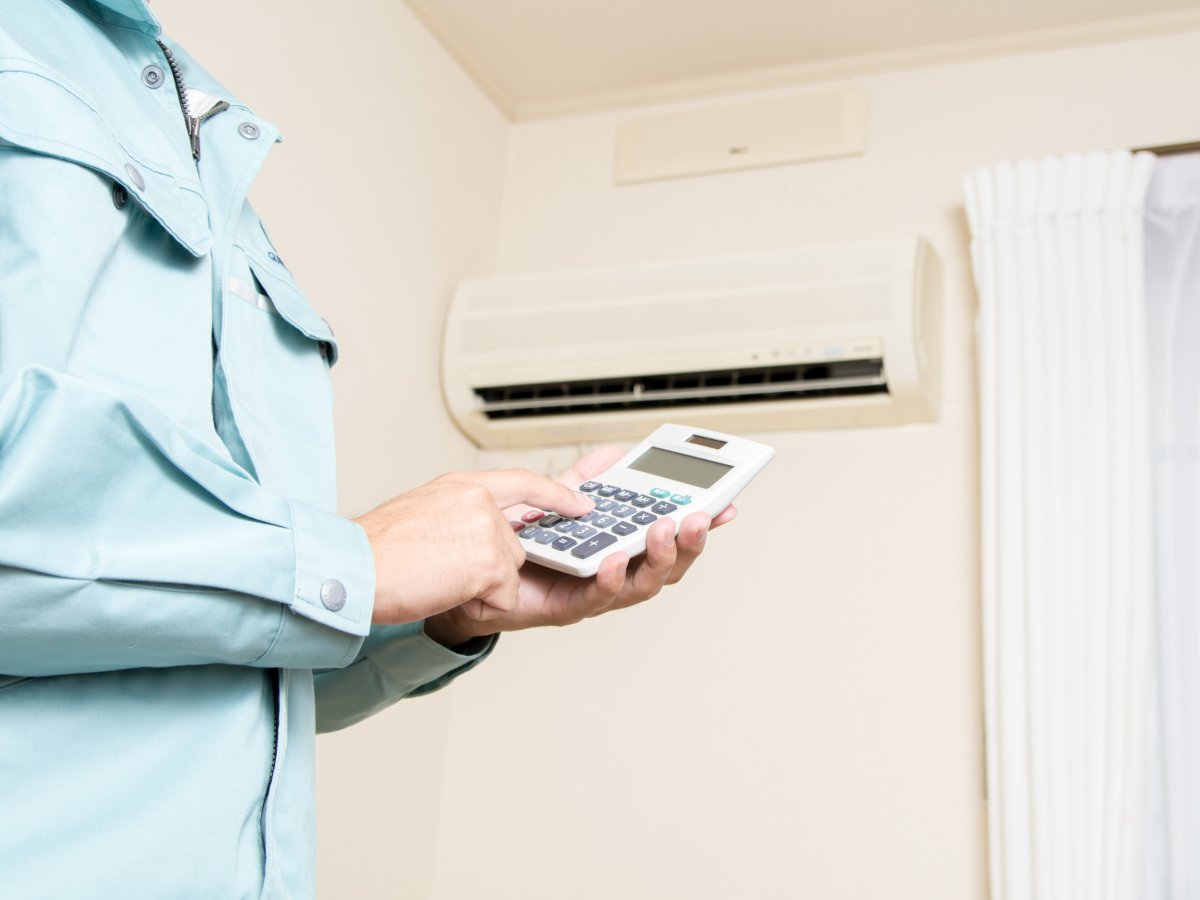 Muškarac stoji ispod klime i drži kalkulator u ruci - inverter klima je štedljiva