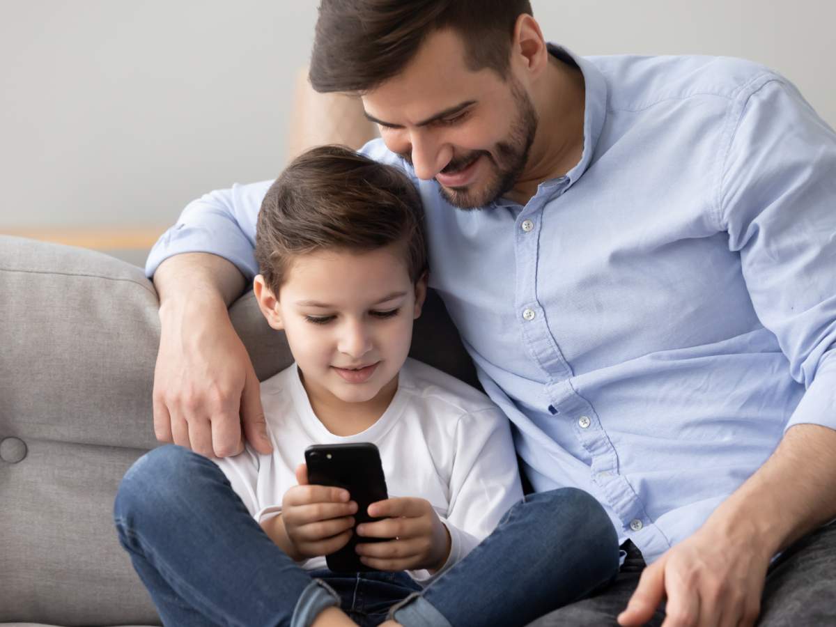 Otac i sin sede na kauču i gledaju video na telefonu