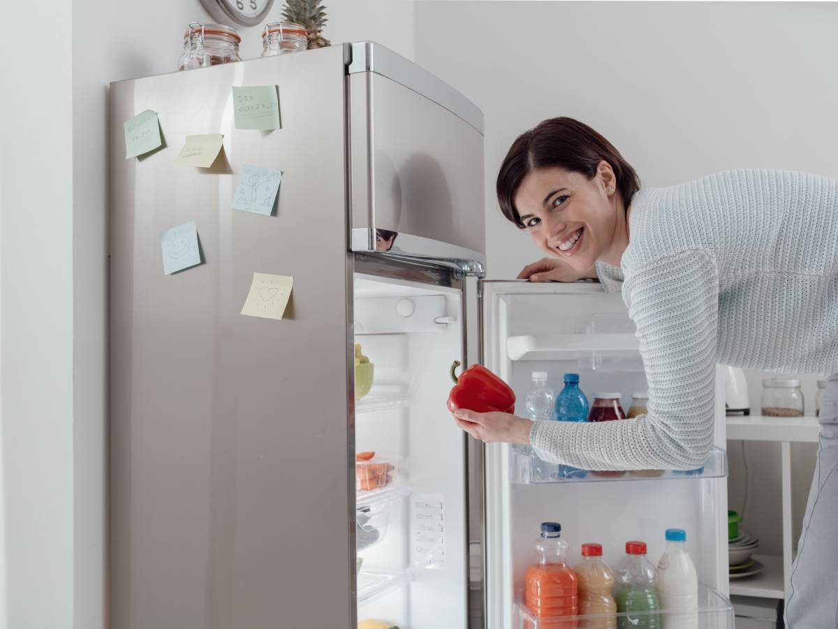 Kombinovani frižider sa otvorenim vratima i devojka koja drži papriku