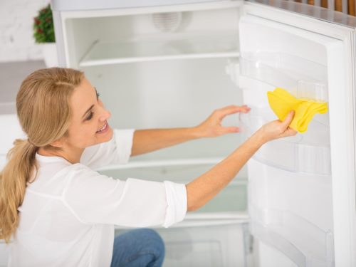 Kako očistiti frižider sirćetom - devojka briše unutrašnjost frižidera