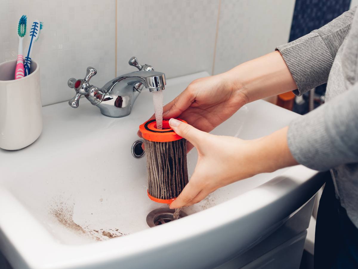 Ženska osoba pere filter usisivača pod mlazom mlake vode