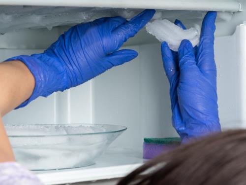 Kako brzo otopiti led u frižideru - ženska osoba sa rukavicama na rukama odvaja komade leda