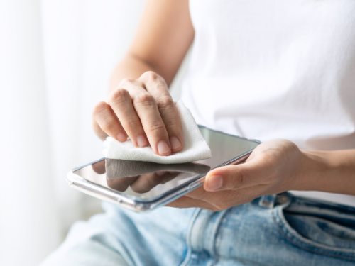 Čišćenje i dezinfekcija mobilnog telefona - osoba briše ekran telefona krpom