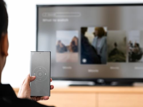 Kako upravljati televizorom preko telefona - muškarac menja kanale telefonom